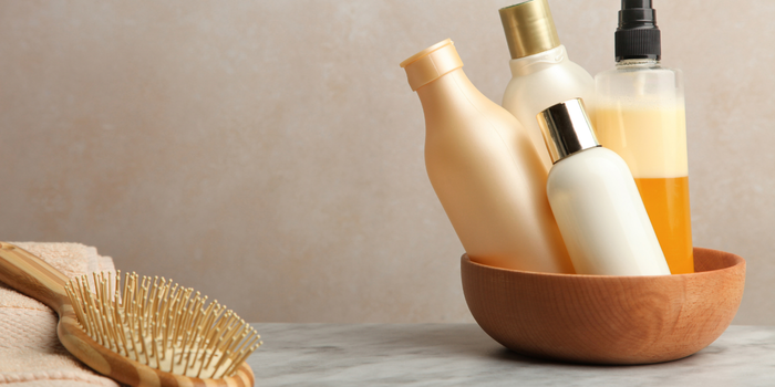 Различные бутылочки с средствами по уходу за волосами в деревянной миске рядом с расческой.