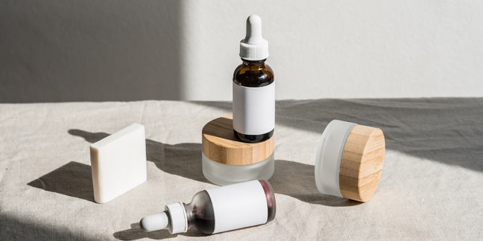 Ahşap kapaklı kozmetik kavanozları ve damlalıklı şişeler, doğal ışıkta sergileniyor.