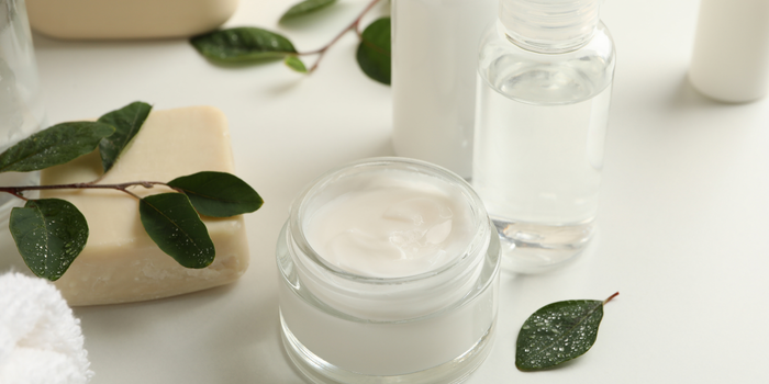 Мыло, натуральные сливки и прозрачные бутылки на однотонном фоне с зелеными листьями (вид сверху).