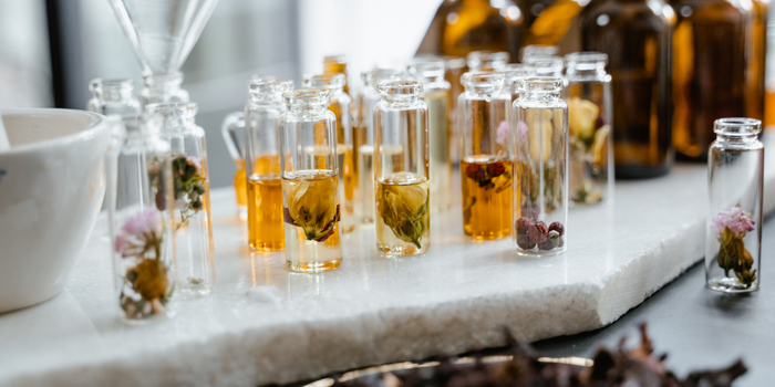 Травяные эссенции и сухоцветы, хранящиеся в различных прозрачных стеклянных бутылках.